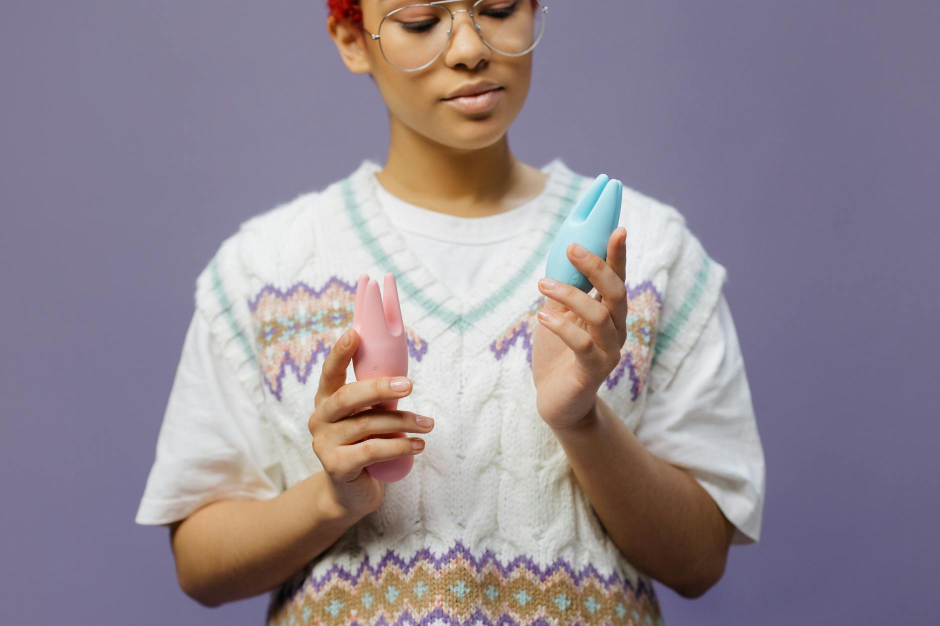 Woman holding blue and pink silicone vibrators, exploring pleasure options thoughtfully