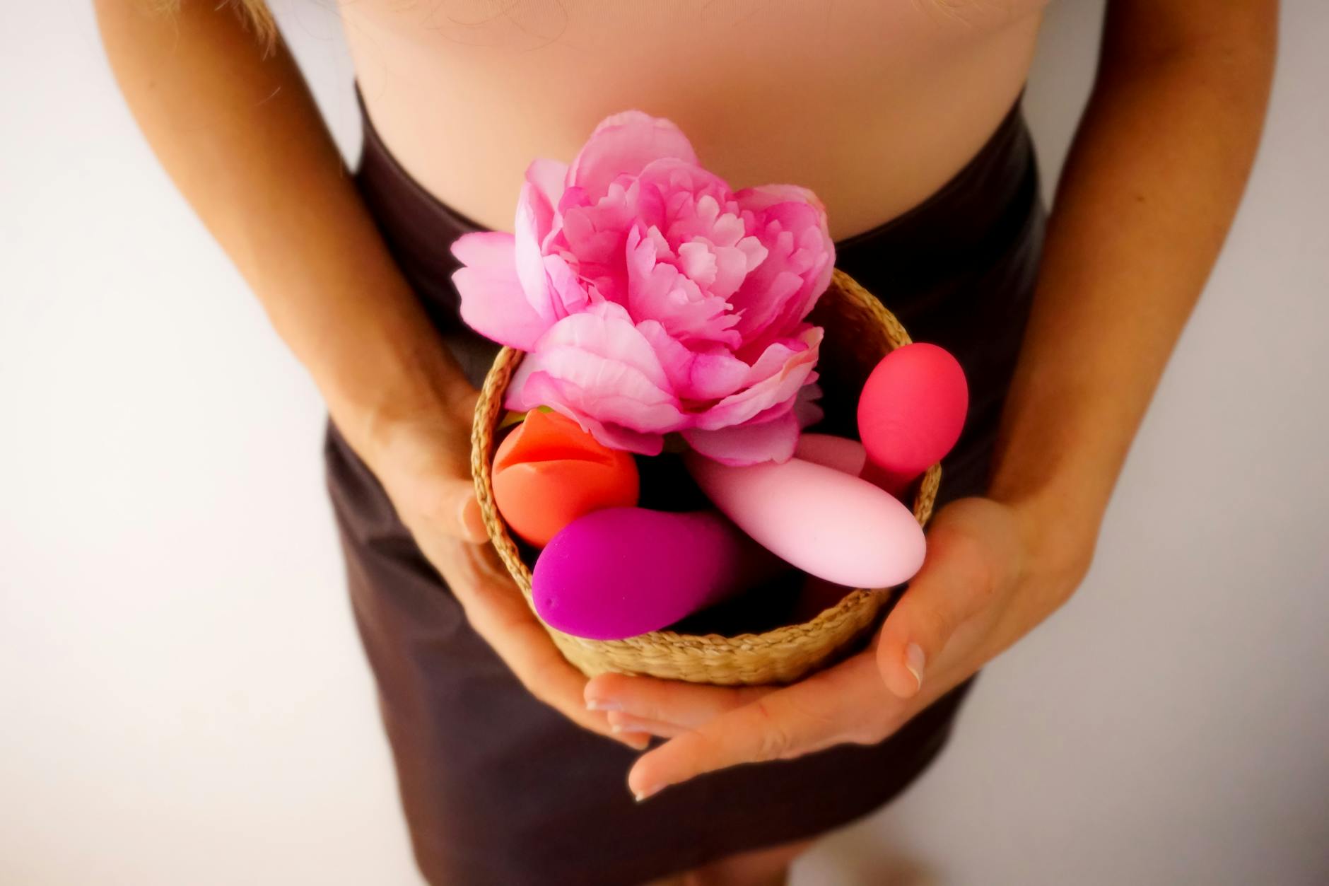 Basket with colorful vibrators and pink flower representing sensual self-care and pleasure.